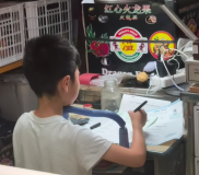 一小學(xué)生在鬧市水果攤寫作業(yè) 專注力引網(wǎng)友熱議