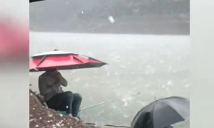 钓鱼人遇冰雹撑伞淡定垂钓：雨雹如蛋！