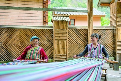 在云南贡山县独龙江乡迪政当村，70多岁的独龙族老人李文仕（左）和女儿一边编织独龙毯一边交流。新华社发