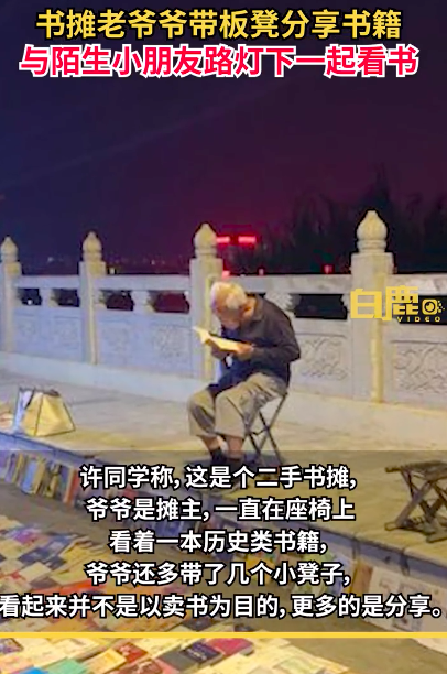 小朋友与书摊爷爷路灯下默契看书 一个探索未来一个品味过去