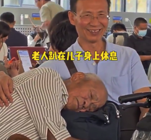 候车时老人枕在儿子怀里安睡 ​网友：老爷爷醒来的那会笑了一下，可爱得像个孩子