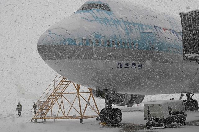 2024年11月27日，韩国仁川国际机场，工作人员在降雪中站在停靠的韩航飞机旁。视觉中国 图