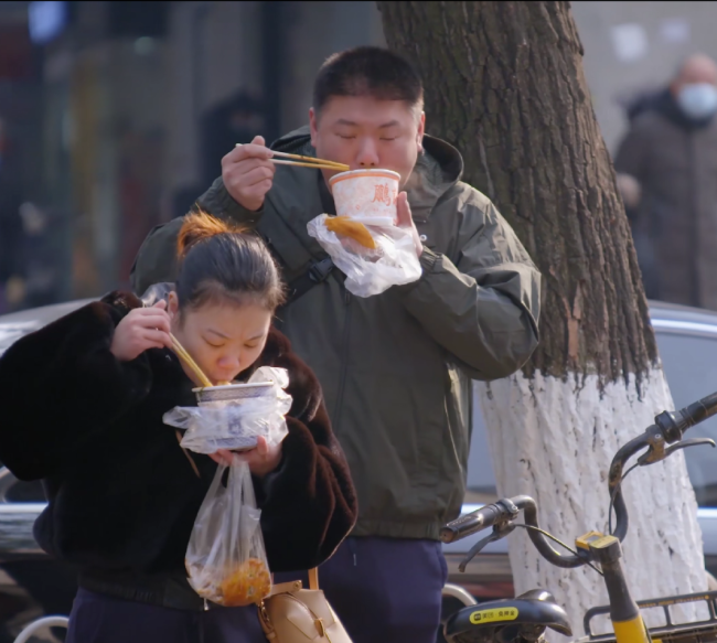 武汉清晨，站在路边吃热干面的上班族。图片来自B站纪录片《第一餐》。