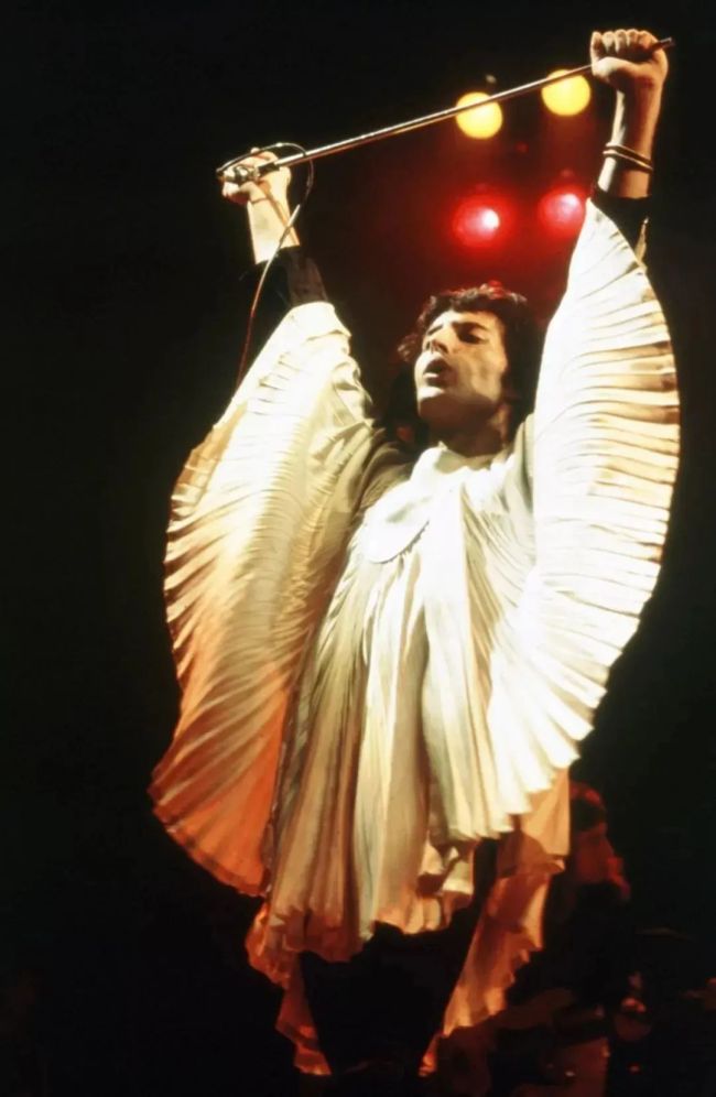 （《一次半埃及式的庄严游行》，大卫·霍克尼，布面油画，1961年）皇后乐队的 Freddie Mercury 和 Brian May 在舞台上身着 Zandra Rhodes 设计的服装, 1974年。摄影：Douglas Puddifoot / Courtesy of Zandra Rhodes<br>
