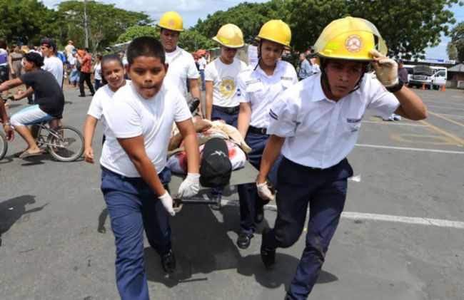 2015年9月22日，尼加拉瓜首都马那瓜，几名小学生在消防员指导下参与地震救援演习。（新华社发，约翰·布斯托斯摄）