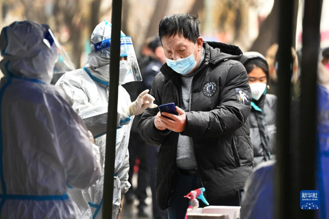 12月25日，防疫人员在西安市新城区皇城西路检测点指导市民扫码检测。