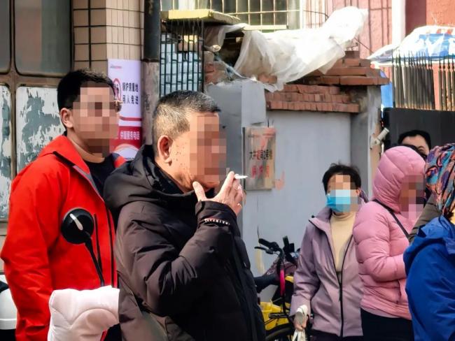 家长等孩子放学校门口抽烟引争议 校门口禁烟难